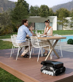 Two people sitting at an outdoor table with an AquaSense 2 Ultra robotic pool cleaner in the foreground.